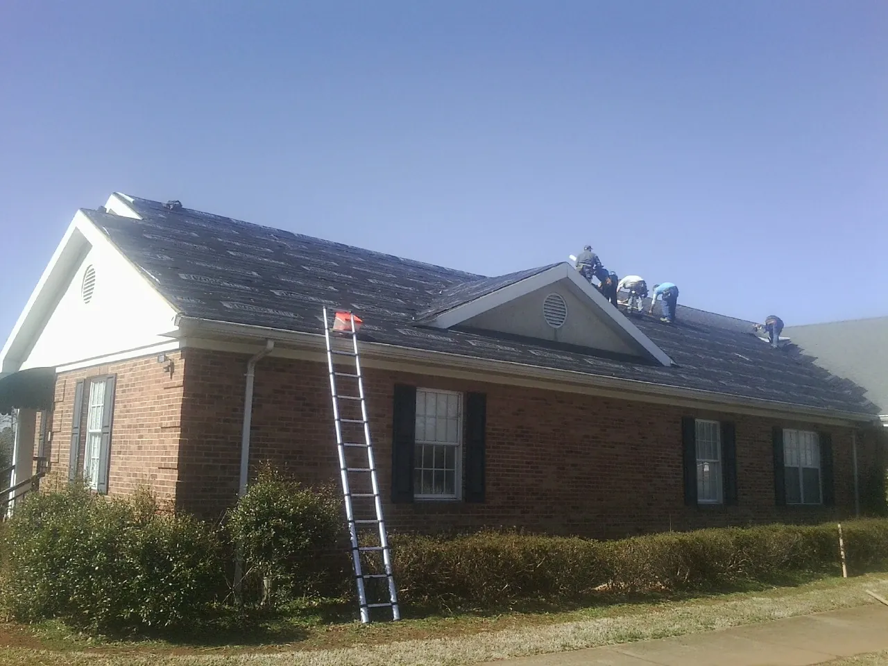 Crew tearing shingles off a brick ranch roof with a ladder set — Metal Roof Repair work by our crew in Snow Hill