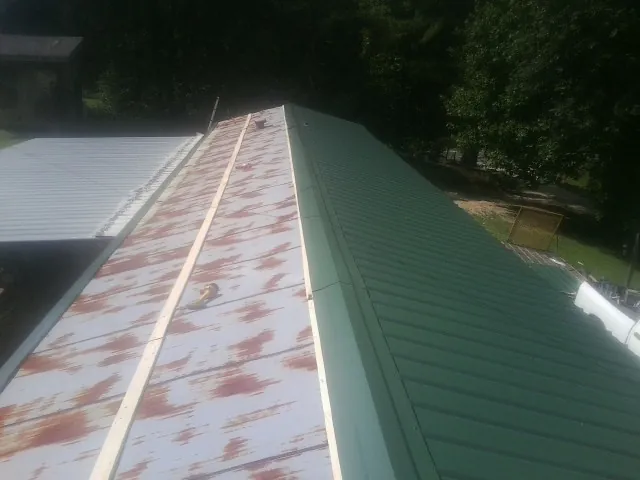 Old rusted panels beside newly installed green metal roofing — Wind Damage Roof Repair by Roofing Brothers in Snow Hill