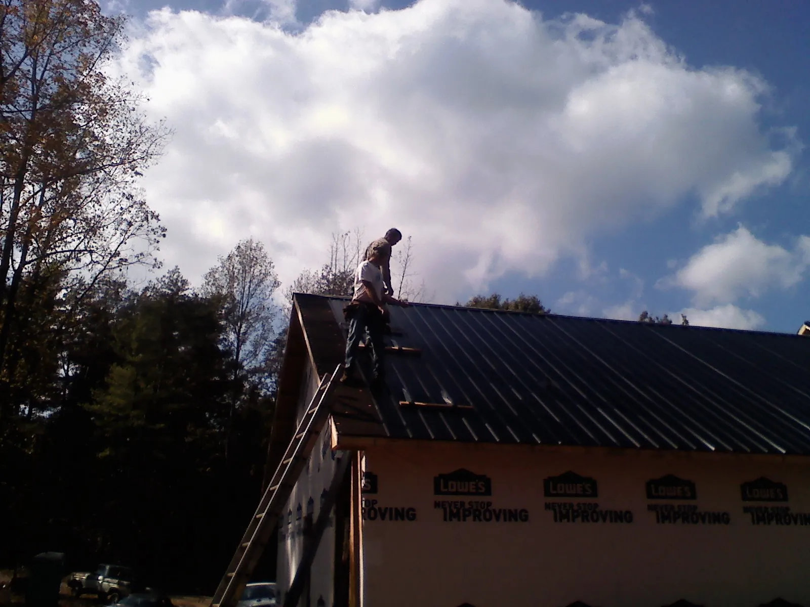 Roofer fastening dark metal panels high against a cloudy sky, from a Roof Inspection job in Snow Hill