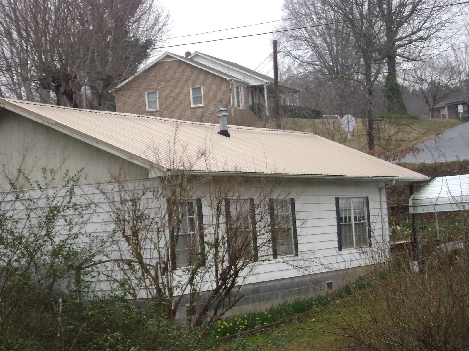 Tan metal roof on a white sided house set into a hillside — Commercial Roofing by Roofing Brothers in Snow Hill